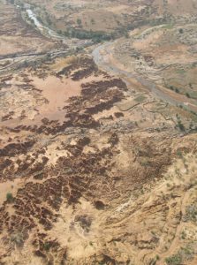 Sur cette photo prise vers l’amont, les ravinements d’Ounjougou sont très reconnaissables dans le secteur de la confluence. On peut également distinguer la terrasse protohistorique (qui domine directement le Yamé) du glacis supérieur (au premier plan à gauche). Photo aérienne D. Gladsteen